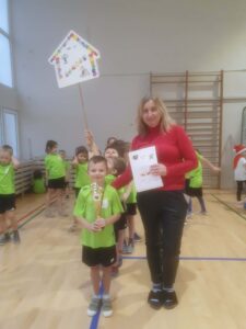 Chłopiec z Panią trzymający puchar oraz dyplom. W tle dzieci