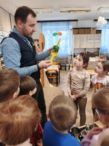 Mężczyzna stojący i trzymający w dłoni wyciskarkę . Wokół stojące dzieci.